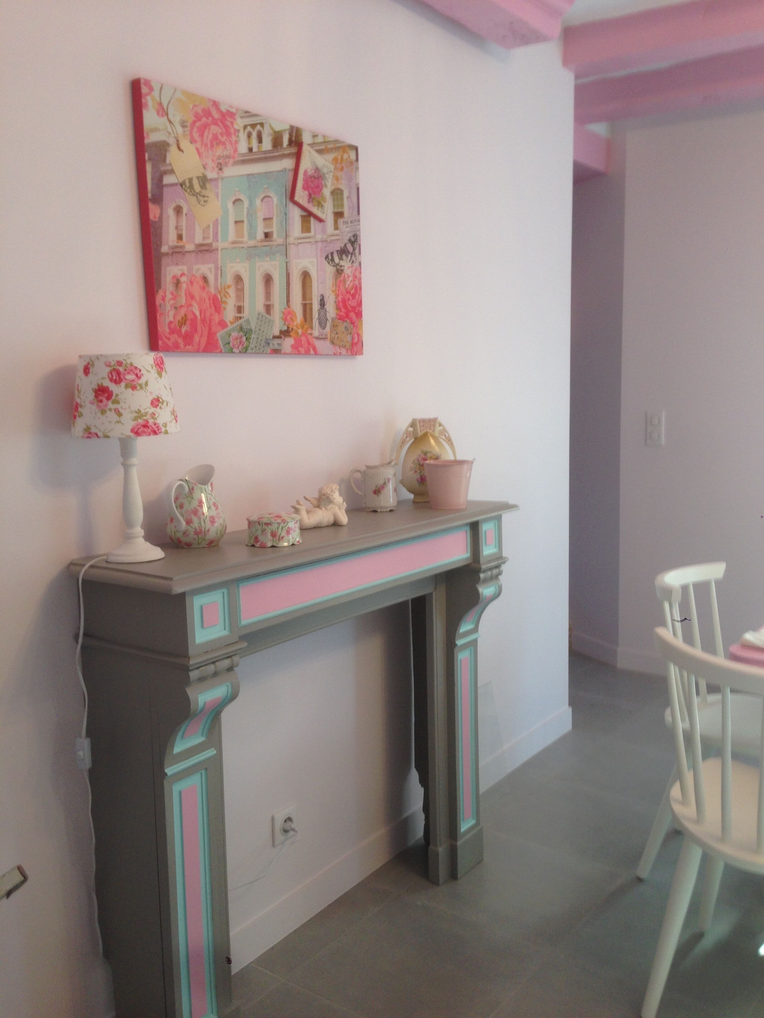 Une pièce avec une console aux couleurs rose et turquoise, une lampe à motifs floraux et un tableau représentant un bâtiment.