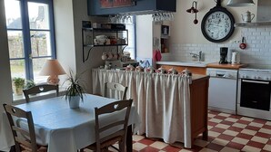 A kitchen with a dining table, chairs, a clock, and a coffee station.