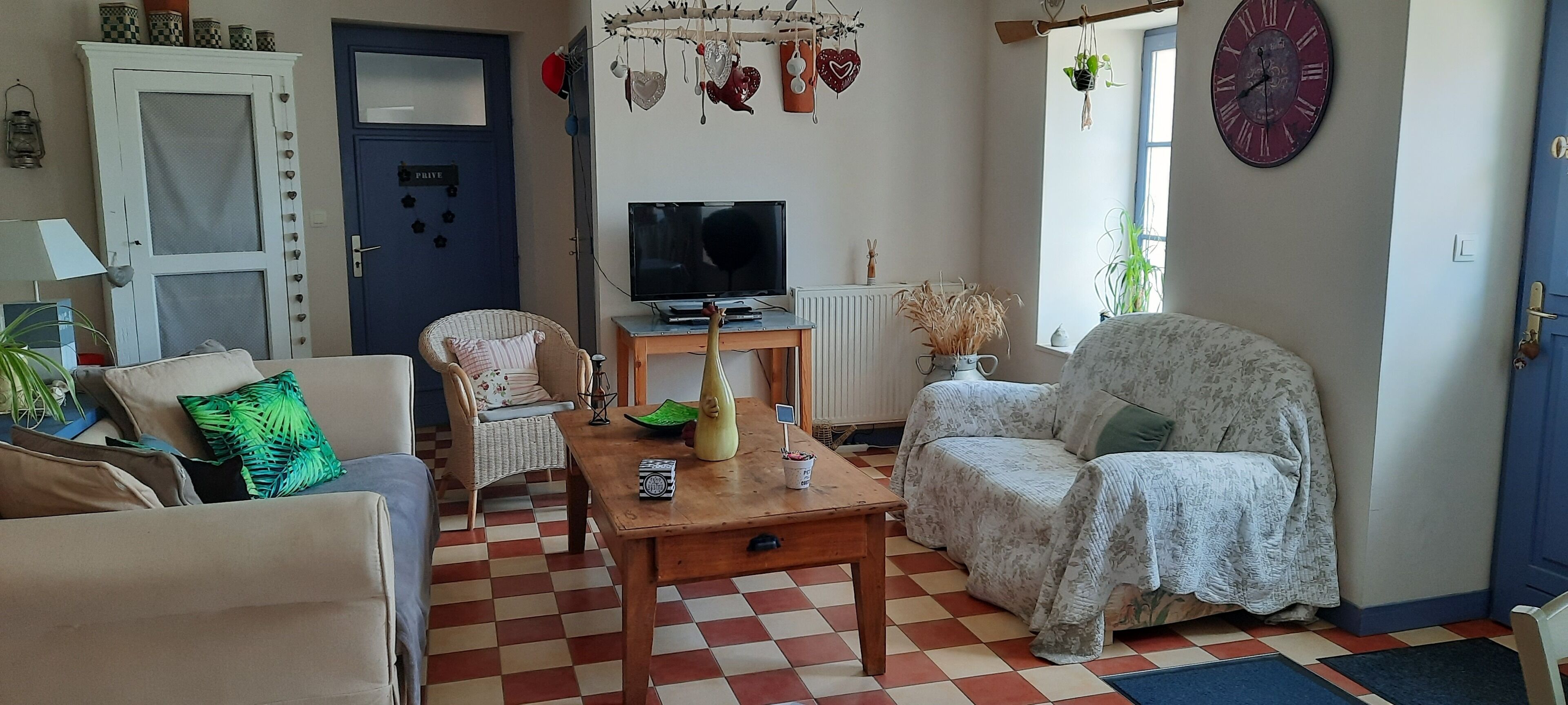 Un soggiorno con pavimento a scacchi, una televisione, un tavolo di legno e un divano.
