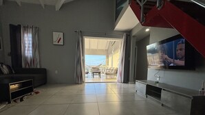 Amplia sala de estar con un televisor grande, un sofá y un comedor visible a través de una puerta abierta.