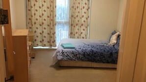 A bedroom with a bed, a dresser, and a window with floral curtains. - Comfy and cozy apartment with two bedrooms  (Birmingham)