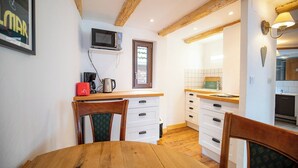 A compact kitchen with wooden beams, a microwave, a coffee maker, and a dining area with a table and chairs. - Les Vignes Vacation Rental - Studio - Route des Vins d'Alsace (Dieffenthal)