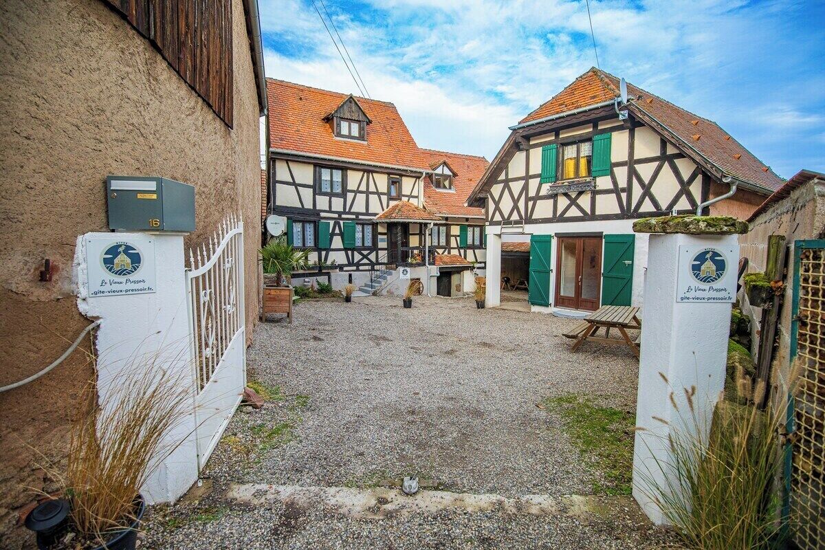 A courtyard with traditional half-timbered houses, a gravel path, and a wooden bench.