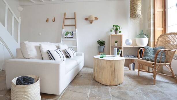 Ein gemütliches Wohnzimmer mit einem weißen Sofa, einem runden Holztisch, einem Korbstuhl und einem Bücherregal.