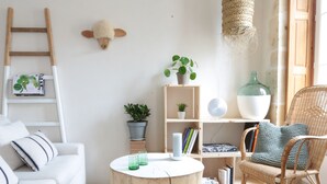 Ein gemütliches Wohnzimmer mit einem weißen Sofa, einem Korbstuhl, einem Holztisch und einem Bücherregal.