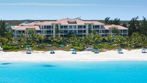 A large resort with multiple buildings, a beach with umbrellas, and palm trees. - Villa Renaissance 402:  4th Floor 2 Bedroom, 2 1/2 Baths Ocean Front Penthouse (Grace Bay)