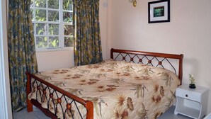 A bedroom with a bed, curtains, a nightstand, and a framed picture on the wall. - Your Perfect Winter GetAway (Rodney Bay)