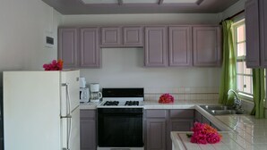 A kitchen with white cabinets, a stove, a refrigerator, and a window with green curtains. - Your Perfect Winter GetAway (Rodney Bay)