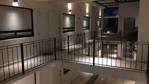 Um saguão de hotel moderno com guarda-corpo de vidro, várias portas e uma escadaria central.
