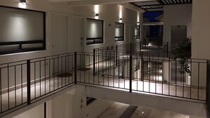 Interior de hotel moderno com um amplo átrio, uma varanda com guarda-corpo e uma televisão de tela plana grande fixada na parede.