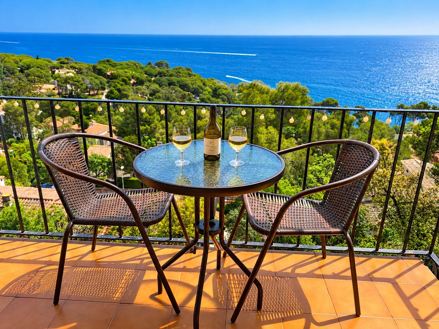 A round table with two chairs on a balcony overlooking a coastal landscape.