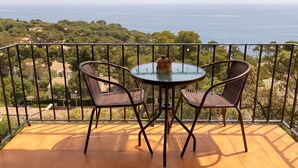 Un balcon avec deux fauteuils en osier et une petite table, offrant une vue panoramique sur la mer et la verdure.