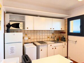 A compact kitchen with white cabinets, a built-in microwave, a sink, and a window with a view. - Beautiful studio in Calella de Palafrugell with sea views! (Palafrugell)