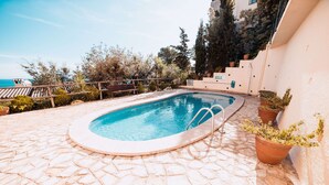 Une piscine dotée d’une terrasse carrelée en pierre, entourée de plantes en pot et offrant une vue dégagée sur la mer.