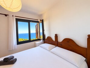 A bedroom with a large window, a wooden bed frame, and a view of the sea. - Beautiful studio apartment with spectacular views of the ocean! (Palafrugell)