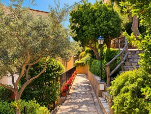 A stone pathway flanked by lush greenery and a wooden staircase. - Beautiful studio in Calella de Palafrugell with sea views! (Palafrugell)