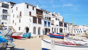 Un bâtiment situé sur la côte, doté de nombreux balcons et d’entrées en arc de cercle, entouré de plusieurs bateaux sur une plage de sable.