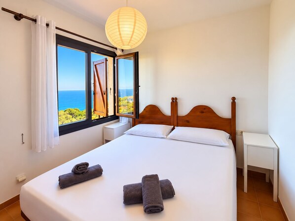 A bedroom with a large bed, two bedside tables, a wooden headboard, a window with curtains, and a hanging light fixture. - Beautiful studio in Calella de Palafrugell with sea views! (Palafrugell)