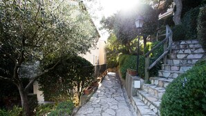 Un chemin de pierre menant à un escalier également en pierre, le tout étant entouré de verdure et bordé d’un bâtiment.