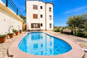 Une piscine bordée de pierres, des plantes en pot et, au fond, un bâtiment doté de nombreuses fenêtres et de balcons.