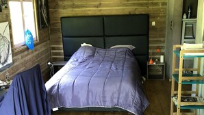 A wooden cabin bedroom with a bed, a desk, and a chair.