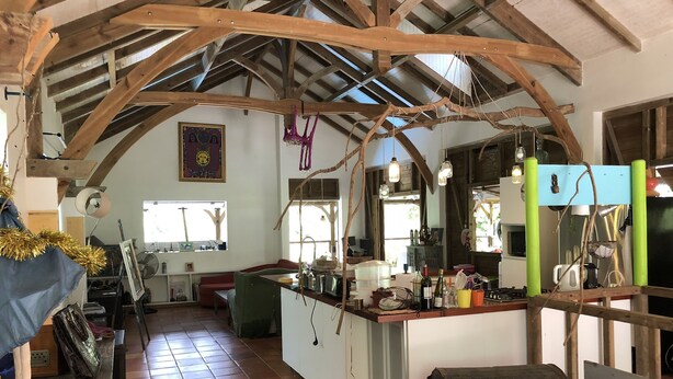 A rustic kitchen with wooden beams, a tiled floor, and a wooden bench.