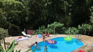 A wooden deck with a swimming pool, lounge chairs, and a red towel.