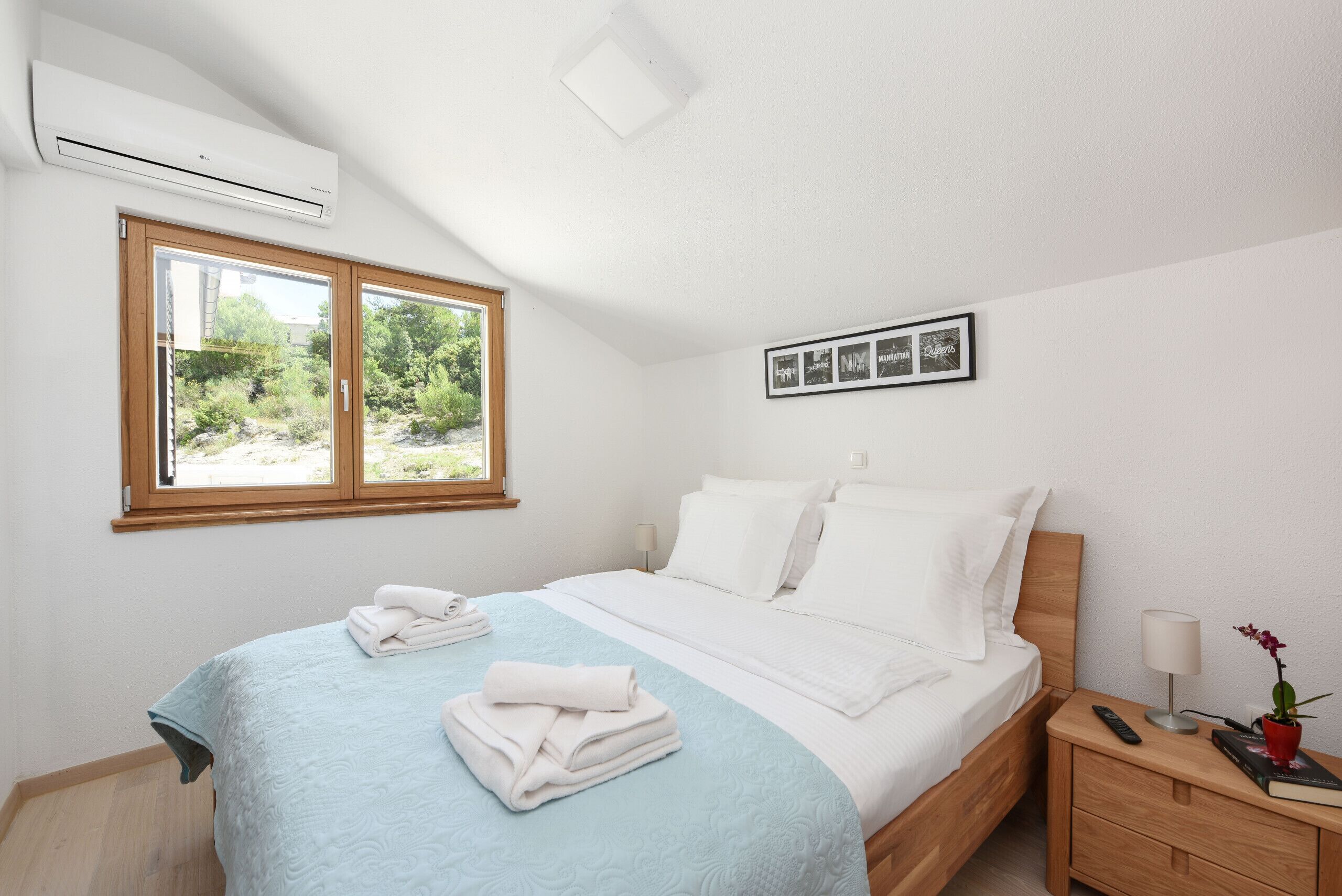 Ein modernes Schlafzimmer mit Bett, Nachttisch, Lampe, Fernbedienung und einem gerahmten Bild an der Wand.