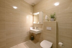 A modern bathroom with a sink, mirror, toilet, and a trash bin.