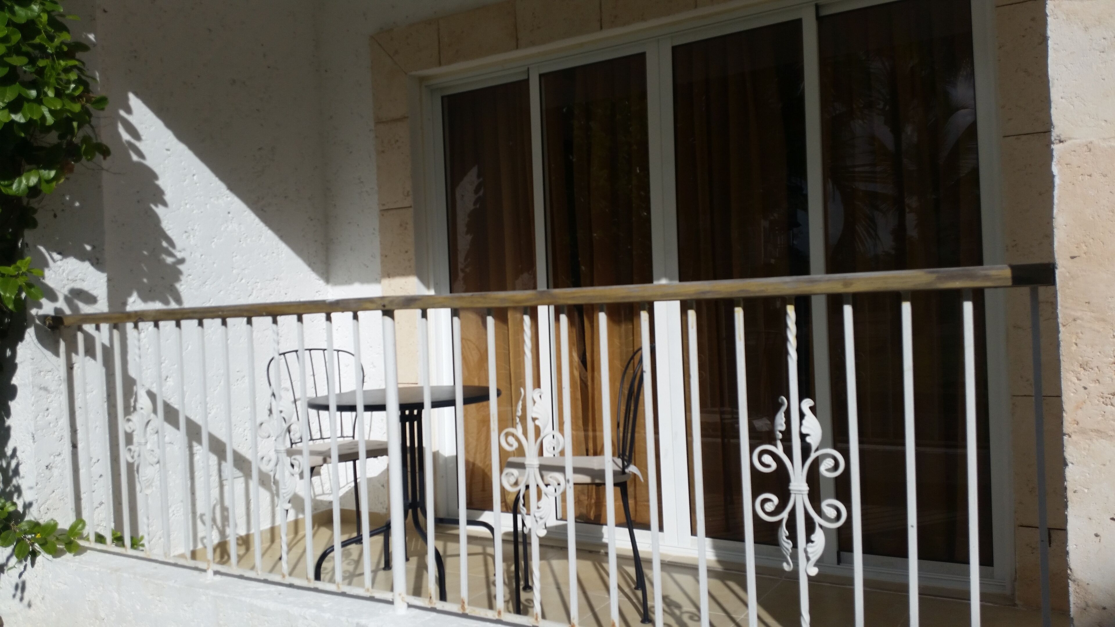 A balcony with a white metal railing, a white chair, and a small table.