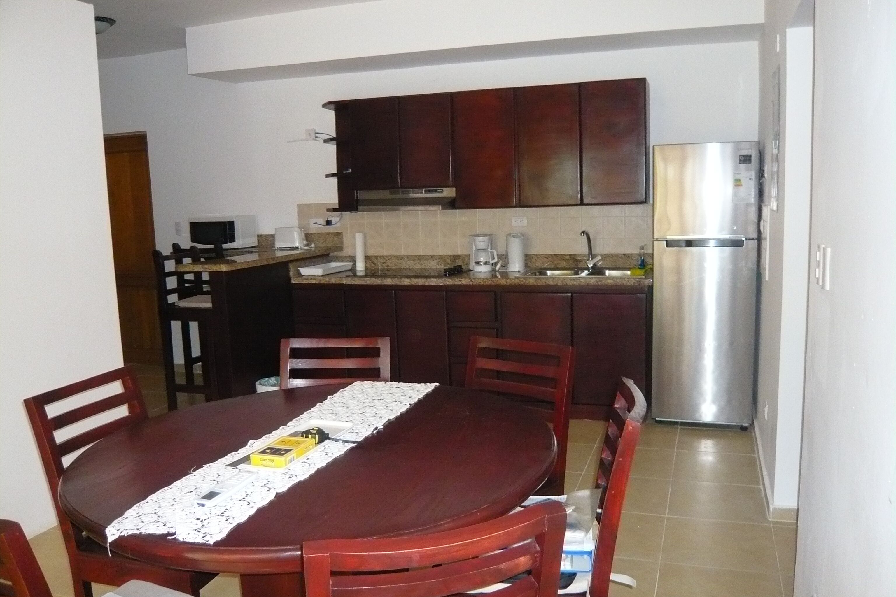 Un comedor con una mesa y sillas de madera, una cocina con armarios de madera oscura y electrodomésticos de acero inoxidable, y un salpicadero de azulejos.