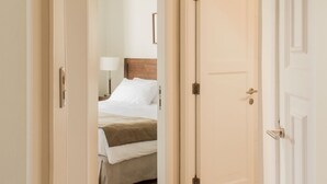 Un couloir d’hôtel menant à une chambre à coucher équipée d’un lit, d’une table de chevet et d’une lampe.