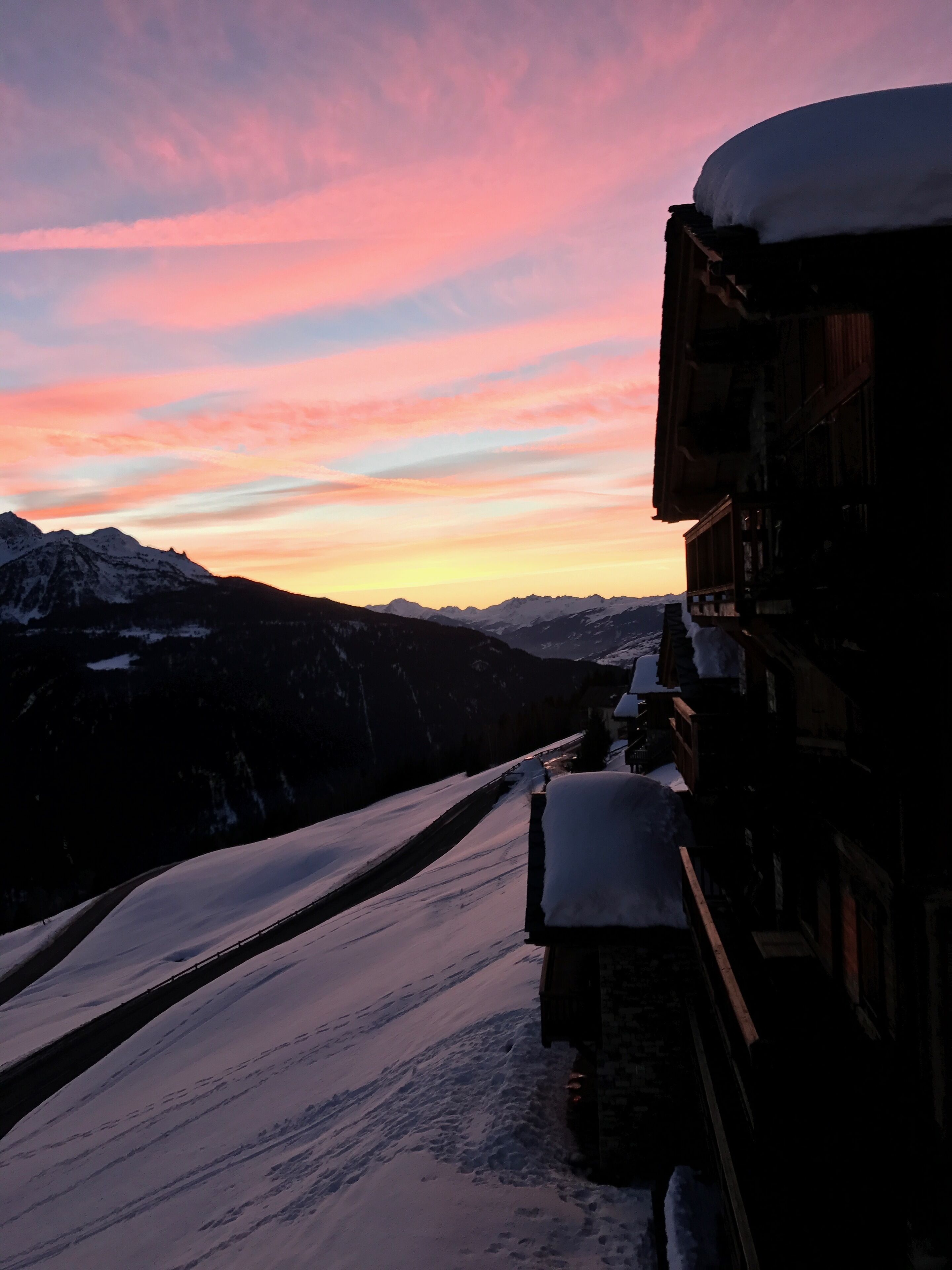 A mountain view with a snow-covered path and a building with a snow-covered roof.
