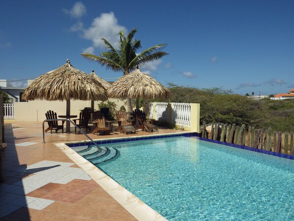A swimming pool with lounge chairs and thatched umbrellas.