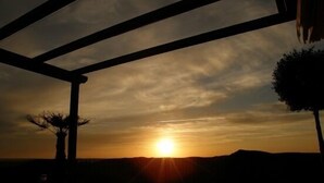 En vacker utsikt över solnedgången från ett takförsett utomhusområde med ett trädäck, stolar och en krukväxt.
