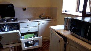 Een functionele keuken met een kookplaat, magnetron, spoelbak en een klein raam.