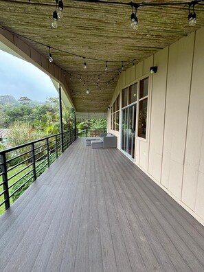 A covered balcony with a wooden floor, large windows, and a view of greenery.
