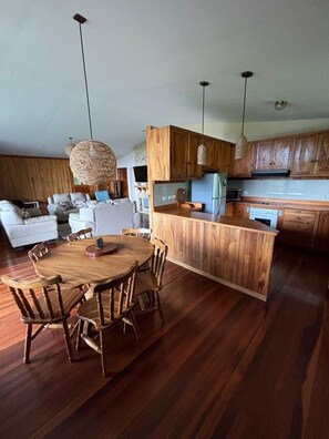 A modern kitchen with wooden cabinets, a central island, and a dining area with a round table and chairs.