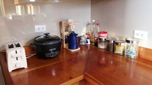 A kitchen with a black slow cooker, a toaster, a wooden shelf with a blue container, and various bottles and jars on the counter. - Perfect house for friends and family in Monteverde (Monteverde)