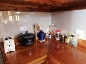 A kitchen with a black slow cooker, a toaster, a wooden shelf with a blue container, and various bottles and jars on the counter. - Perfect house for friends and family in Monteverde (Monteverde)