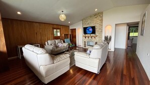 A spacious living room with a stone fireplace, a flat-screen TV mounted above it, and a wooden accent wall. - Perfect house for friends and family in Monteverde (Monteverde)
