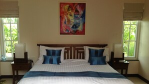 Una cama bien hecha con ropa de cama blanca y azul, dos mesitas de noche con lámparas, un cuadro en la pared y ventanas con persianas.