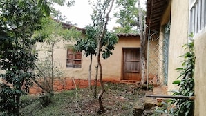 A rustic building with a red brick base and a beige upper structure. There are two windows with wooden shutters, and a small tree in front of the building. - Great view and clean air (Barichara)