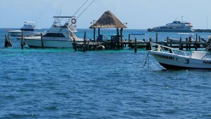 Un puerto deportivo con varias embarcaciones amarradas, una estructura con techo de paja y un gran barco al fondo.