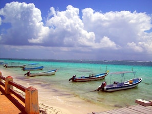 Une plage où plusieurs bateaux sont amarrés près du rivage, avec une promenade en bois et une vue dégagée sur l’océan.