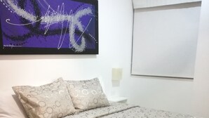 Una cama bien hecha con una colcha estampada, una toalla enrollada y una obra de arte en la pared de arriba.