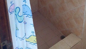 A shower area with a tiled wall, a showerhead, and a curtain with a whale pattern. - Airconditioned room wit kitchnette ideal for individual, family and groups. (Grand Bay)