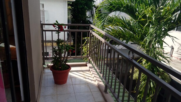 A balcony with a potted plant, a metal railing, and a view of a building and greenery. - Airconditioned room wit kitchnette ideal for individual, family and groups. (Grand Bay)