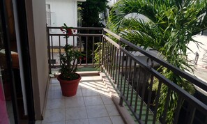 A balcony with a potted plant, a metal railing, and a view of a building and greenery.