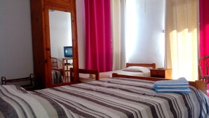 A bedroom with a bed, a chair, a desk with a computer, and curtains. - Airconditioned room wit kitchnette ideal for individual, family and groups. (Grand Bay)